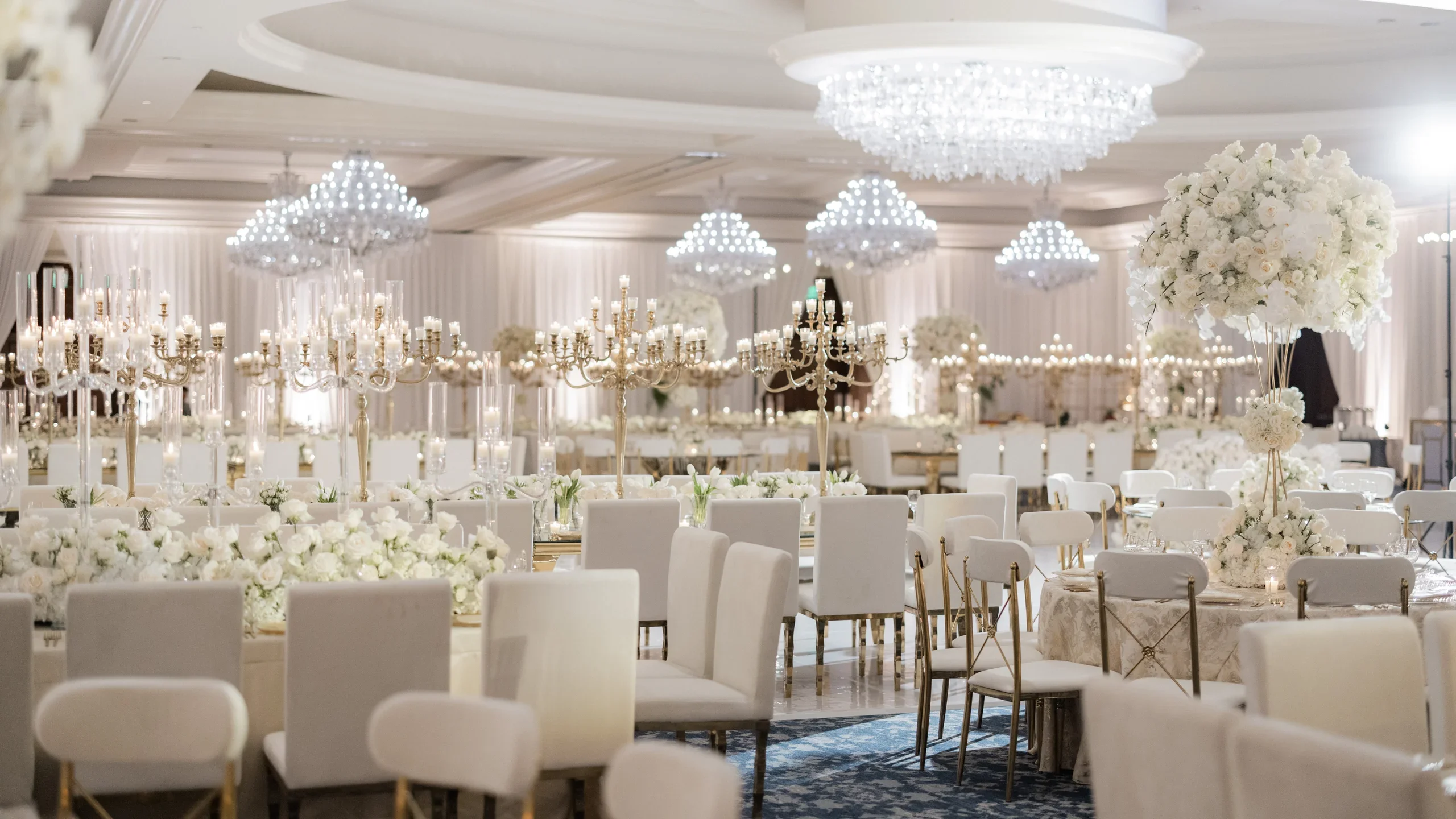 All-white wedding reception with crystal chandeliers, gold candelabras and white florals in the Four Seasons Hotel Westlake Village ballroom